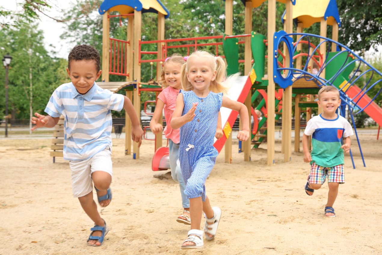 Kinder spielen auf einem bunten Spielplatz mit modernen Spielplatzgeraeten im Freien und trainieren dabei Motorik und Sozialverhalten