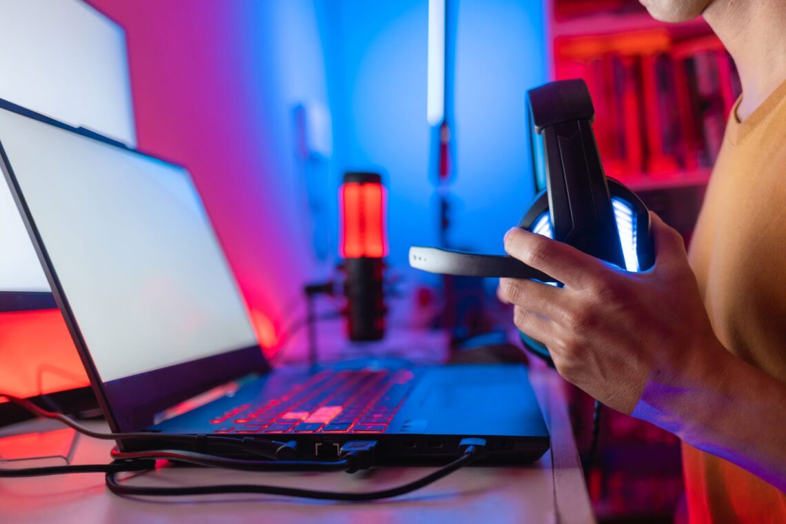 Person hält Gaming-Headset vor beleuchtetem Laptop in rot-blauer RGB-Umgebung