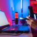 Person hält Gaming-Headset vor beleuchtetem Laptop in rot-blauer RGB-Umgebung