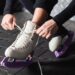 Person bindet Schlittschuhe Bauer mit Kufenschonern auf schwarzem Gummiboden vor der Eisflaeche