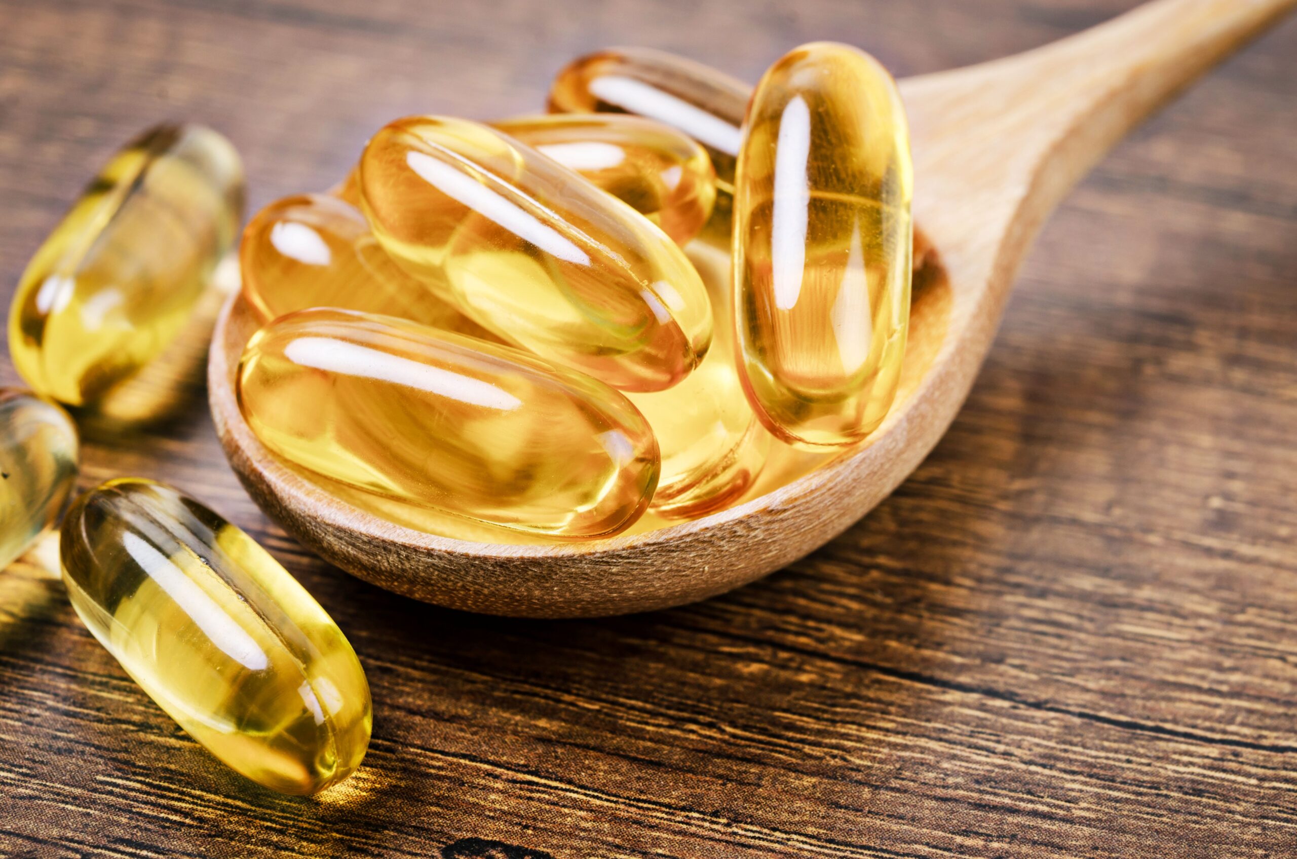 Kapseln mit Omega-3 Algenöl auf Holzlöffel als pflanzliche Nahrungsergänzung