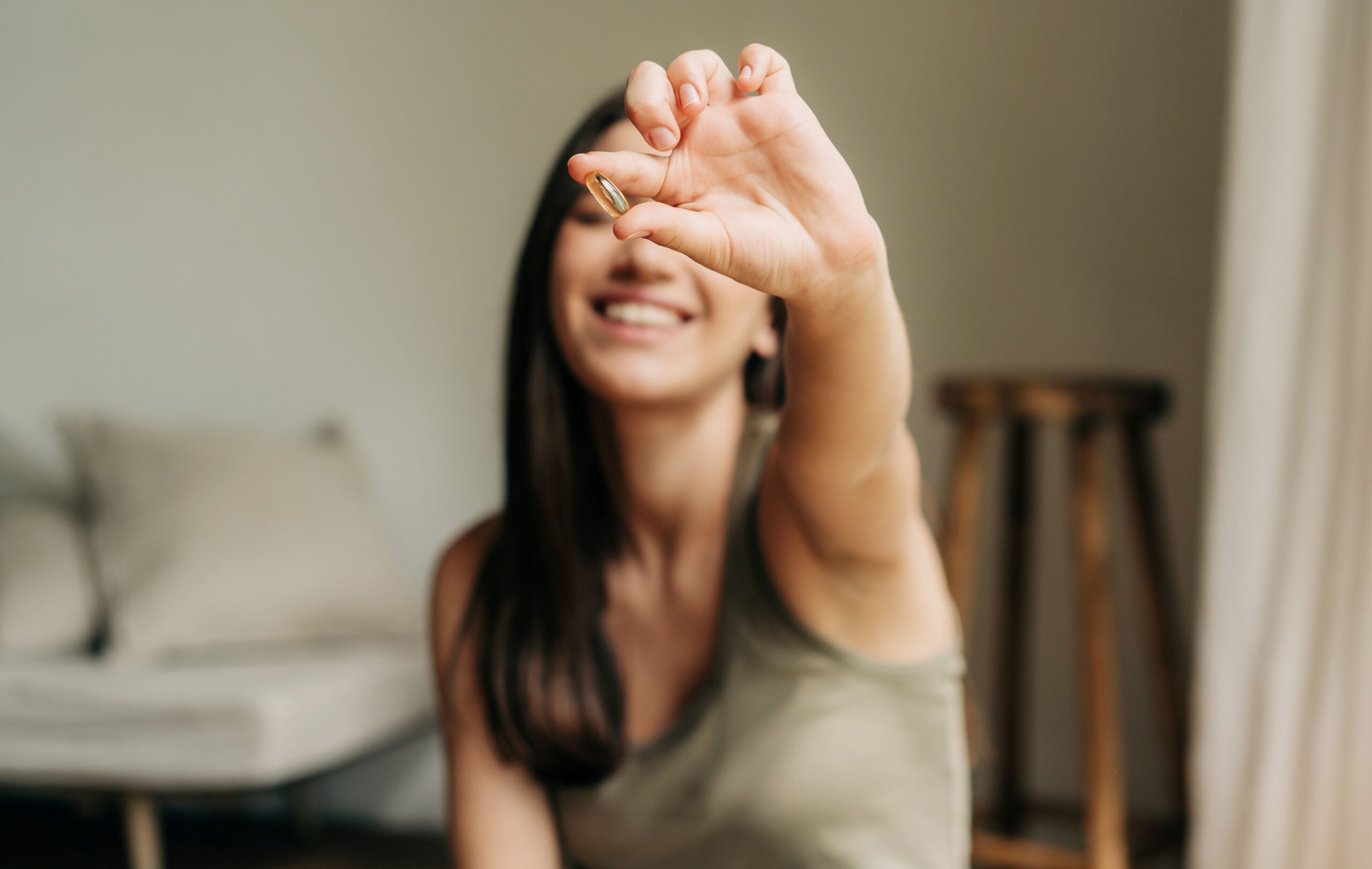 Frau hält eine Omega-3 Algenöl-Kapsel in die Kamera und lächelt entspannt